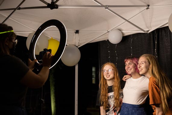 Three students posing for a photo in front of ring light with balloons in the background